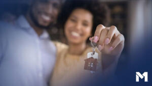 Two people holding up a set of keys with a house-shaped keychain attached to it, likely the keys to their new home.