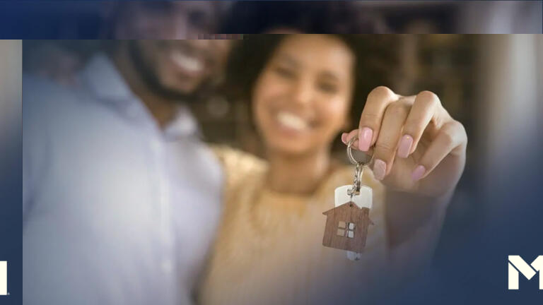 Two people holding up a set of keys with a house-shaped keychain attached to it, likely the keys to their new home.