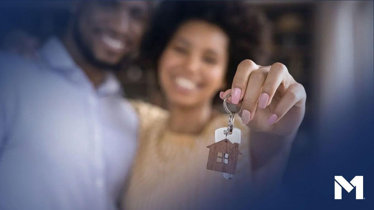 Two people holding up a set of keys with a house-shaped keychain attached to it, likely the keys to their new home.